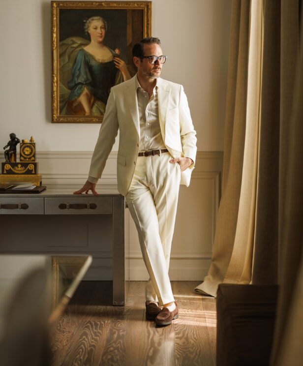 Ivory twill suit with cream shirt and brown suede loafers, worn by a model by a desk