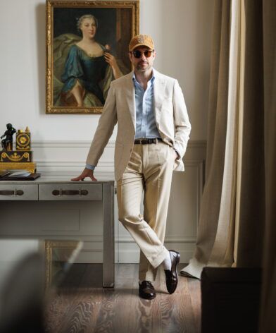 Tan glen plaid blazer with blue shirt and cream trousers, worn by a model by a desk