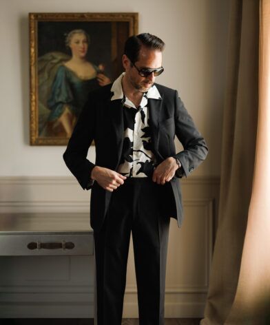 Black suit with a black and white printed camp shirt, worn by a model in a panelled room