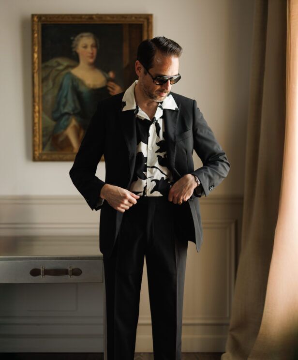 Black suit with a black and white printed camp shirt, worn by a model in a panelled room
