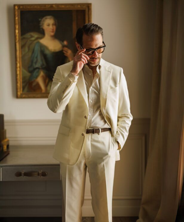 Ivory twill suit with a cream stand collar shirt, worn by a model by a window