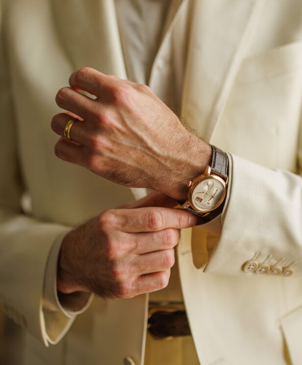 Ivory twill suit cuff with a rose gold watch on a brown strap, a close-up of the wrist