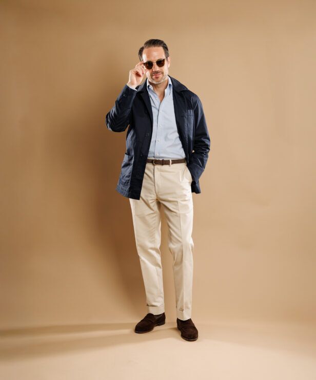Navy chore coat with pale blue shirt, cream trousers and brown suede loafers, full length