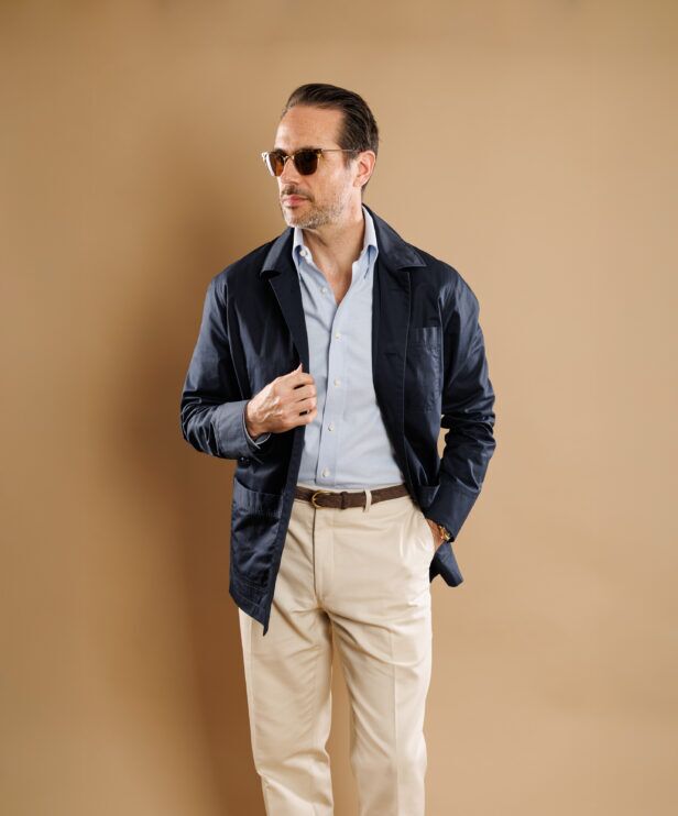 Navy cotton chore coat over a pale blue shirt with cream trousers, worn by a model