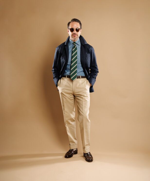 Navy chore coat with chambray shirt, green striped tie and khakis, worn by a model, full length