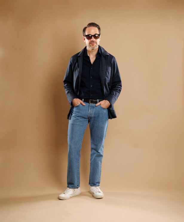 Navy chore coat over a navy shirt with light jeans and white trainers, worn by a model