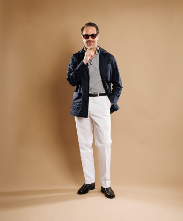 Navy chore coat with grey polo, white trousers and black loafers, worn by a model, full length