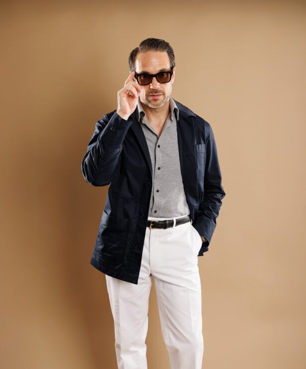 Navy cotton chore coat over a grey polo with white trousers, worn by a model