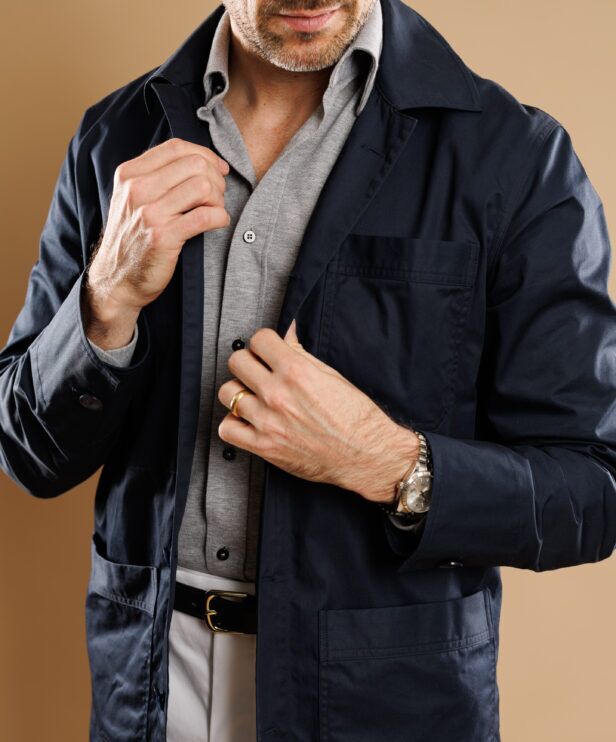 Navy cotton chore coat over a grey polo, a close-up of the chest pocket and cuff