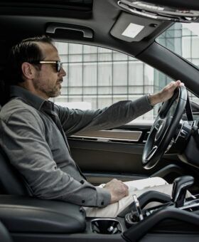 Grey knit polo shirt with cream trousers, worn by a model driving a car