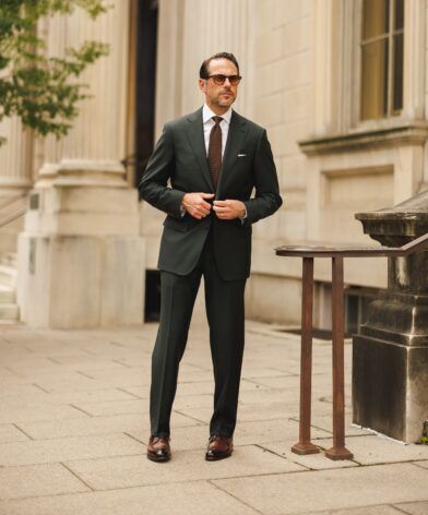 Dark green wool suit with white shirt and brown medallion tie, worn by a model on a pavement