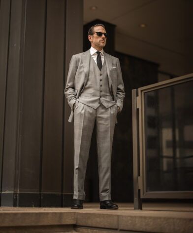 Grey glen plaid three-piece suit with white shirt and black knit tie, worn by a model