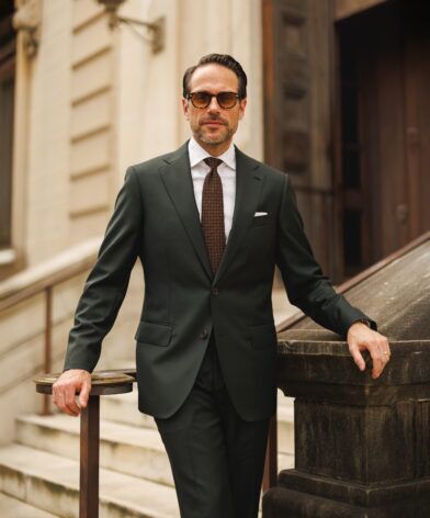 Dark green wool suit with white shirt and brown medallion tie, worn by a model on steps