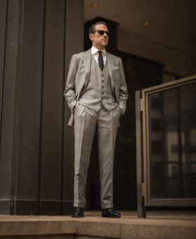 Light grey three-piece wool suit with white shirt, black knit tie and black oxfords, worn by a model