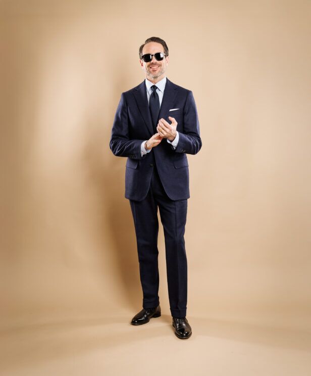 Navy flannel suit with blue striped shirt, navy tie and white pocket square, worn by a model