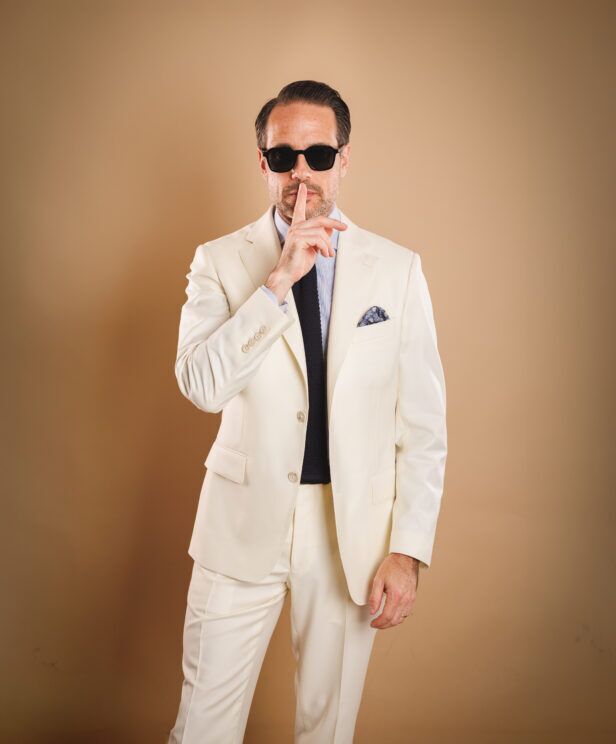Ivory two-button suit with blue shirt, navy knit tie and floral pocket square, worn by a model