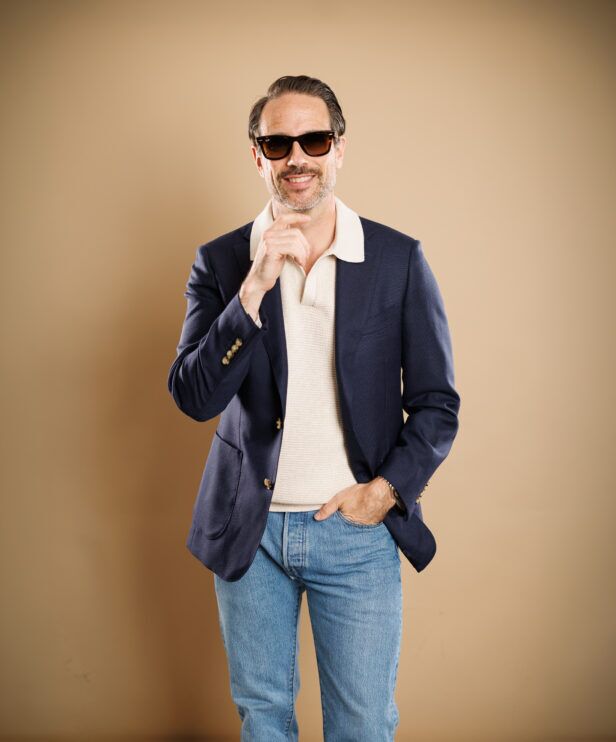 Navy hopsack sport coat with gold buttons, cream knit polo and light wash jeans, worn by a model