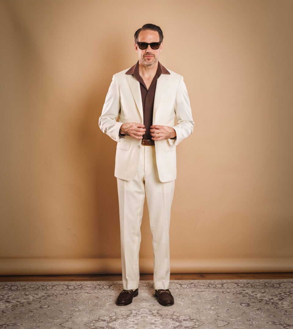 Ivory two-piece suit with brown knit polo and brown bit loafers, worn by a model