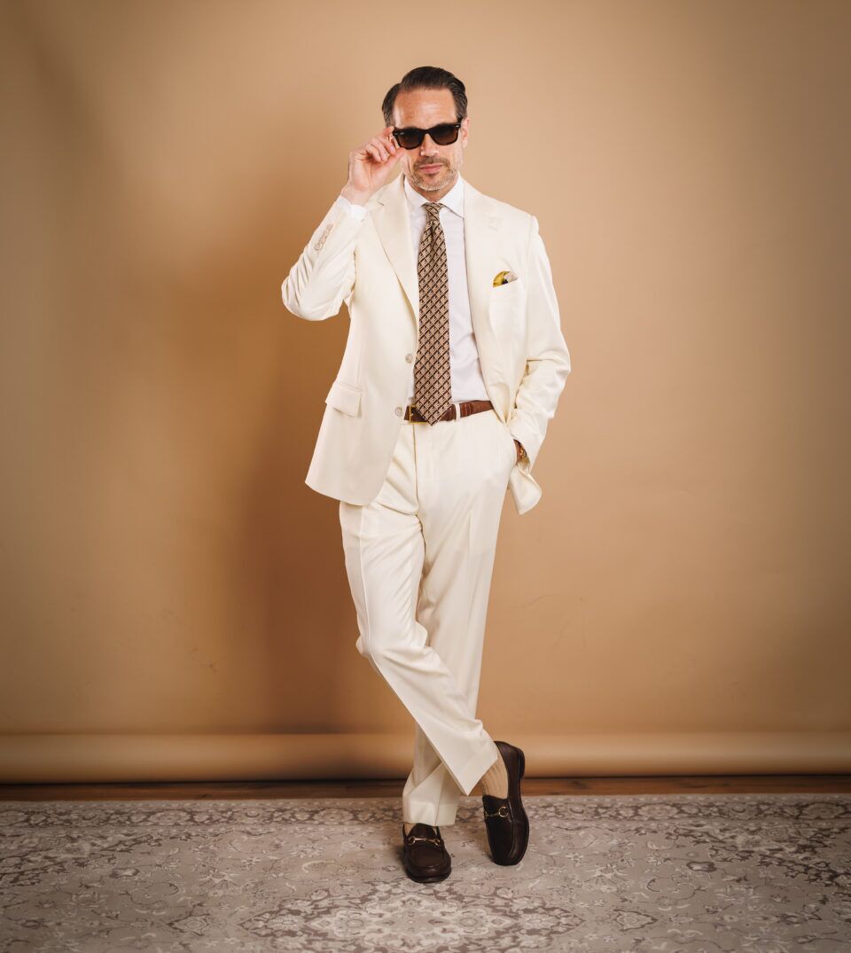 Ivory two-button suit with white shirt, brown geometric silk tie and brown bit loafers, worn by a model