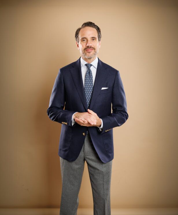Navy hopsack blazer with blue medallion tie, white shirt and grey flannel trousers, worn by a model