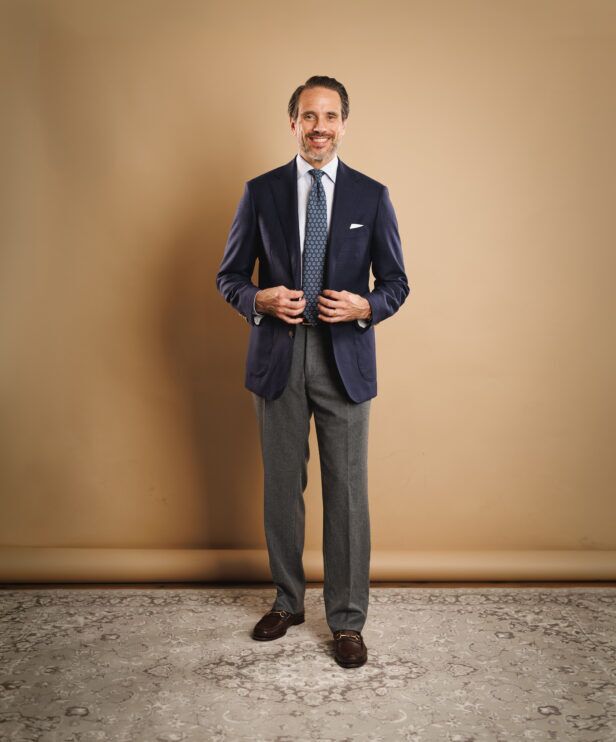 Navy hopsack blazer with white shirt, blue medallion tie, grey flannel trousers and brown loafers, worn by a model