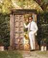 Ivory suit with white shirt, patterned tie and brown loafers, worn by a model by a garden gate